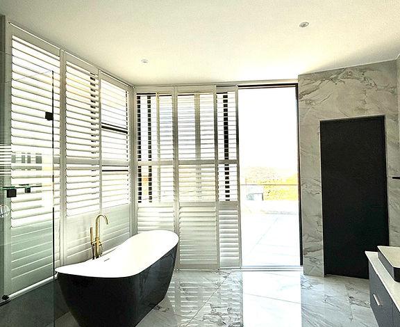 Luxury bathroom with shutters and a freestanding bath in sunlight