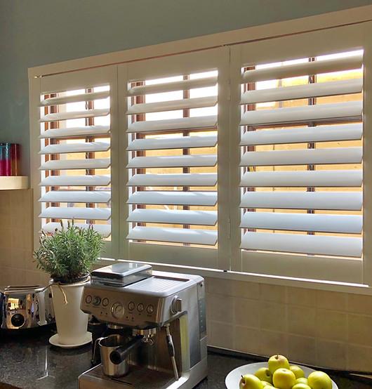 Hinged shutters tilted open above a sunlit kitchen counter